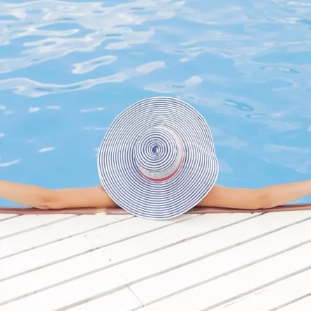 Woman relaxes in pool wearing large stripy sun hat