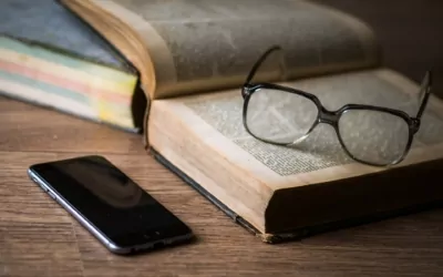 Glasses resting on an open book next to a phone