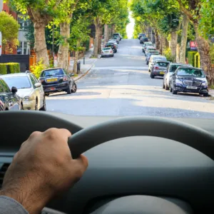Image from drivers perspective with top of wheel in the foreground and road ahead, including signs, clearly visible, with distinct outlines and vivid colours to show significantly improved vision without cataracts/after cataract surgery